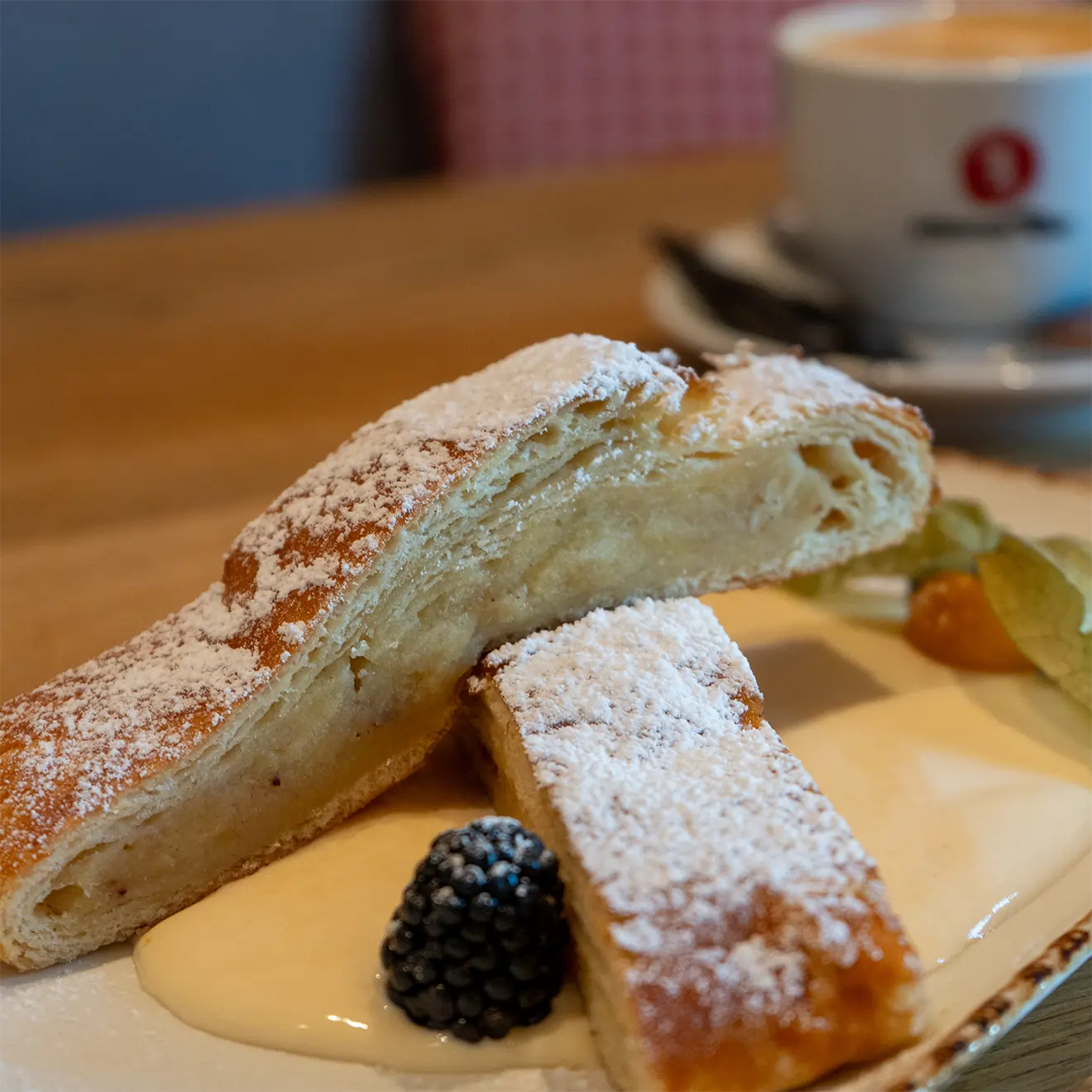 Apfelstrudel auf Vanillesoße, im Hintergrund ein Cappuccino
