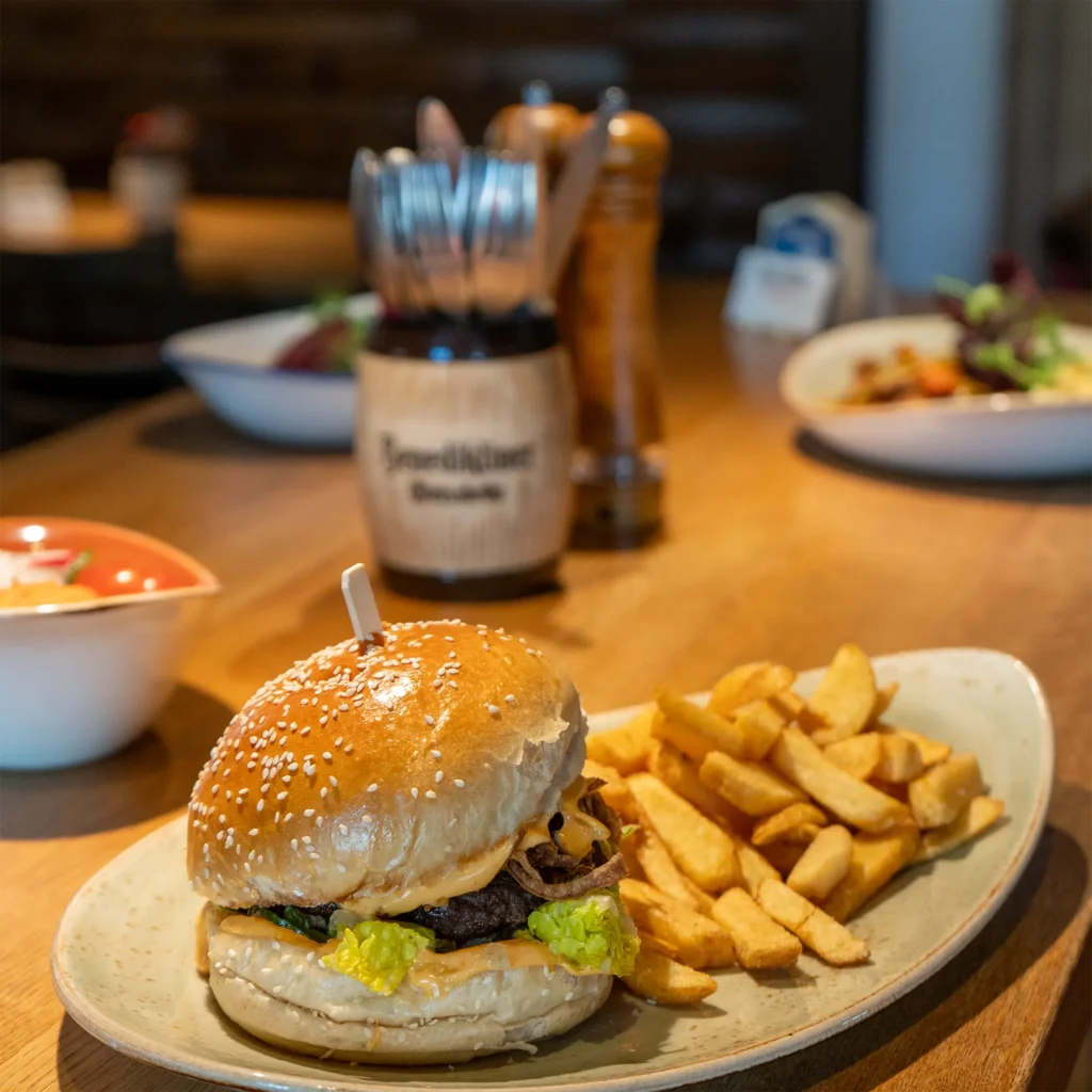 Verschiedene Gerichte auf dem Tisch mit Besteck, im Fokus steht ein Burger mit Pommes
