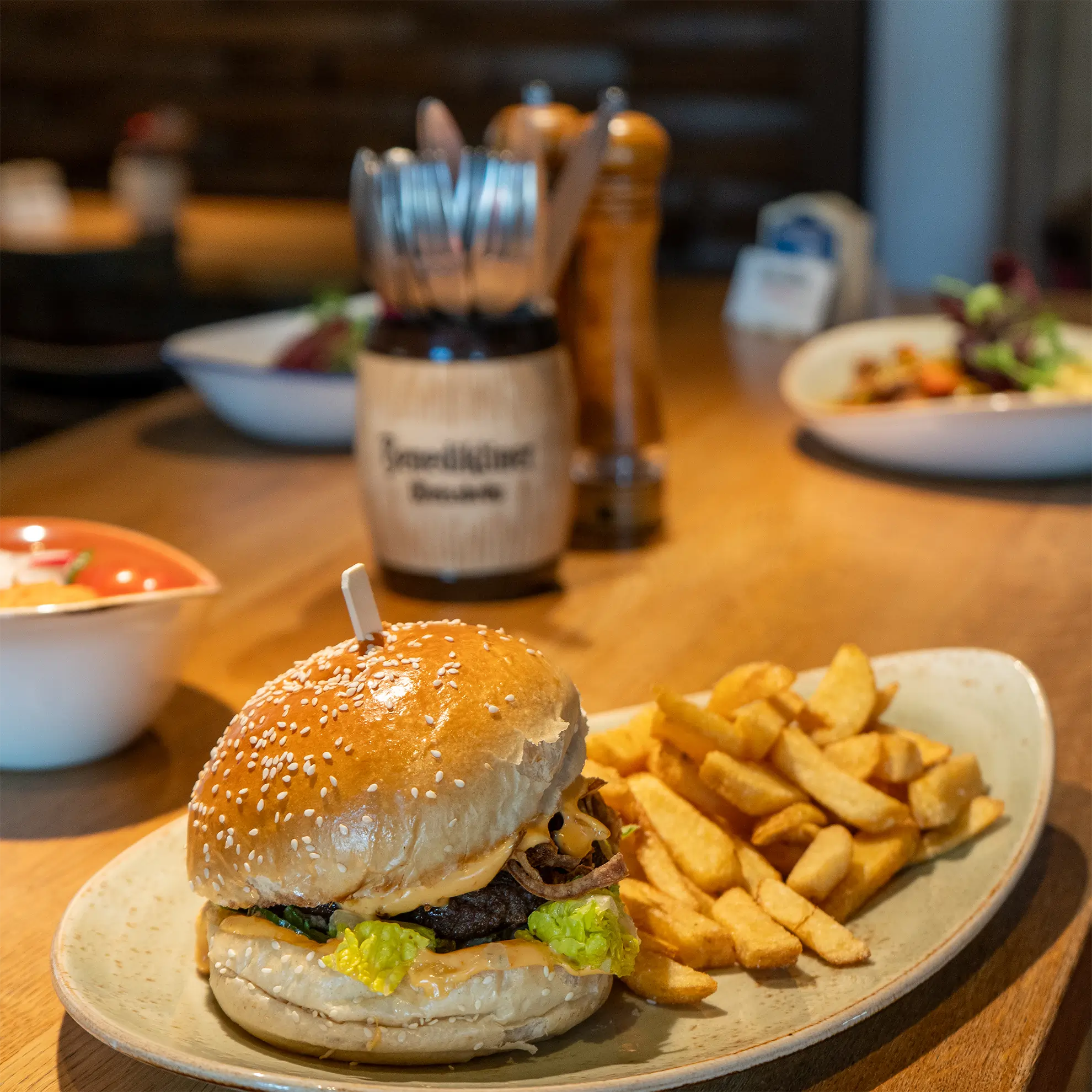 Verschiedene Gerichte auf dem Tisch mit Besteck, im Fokus steht ein Burger mit Pommes
