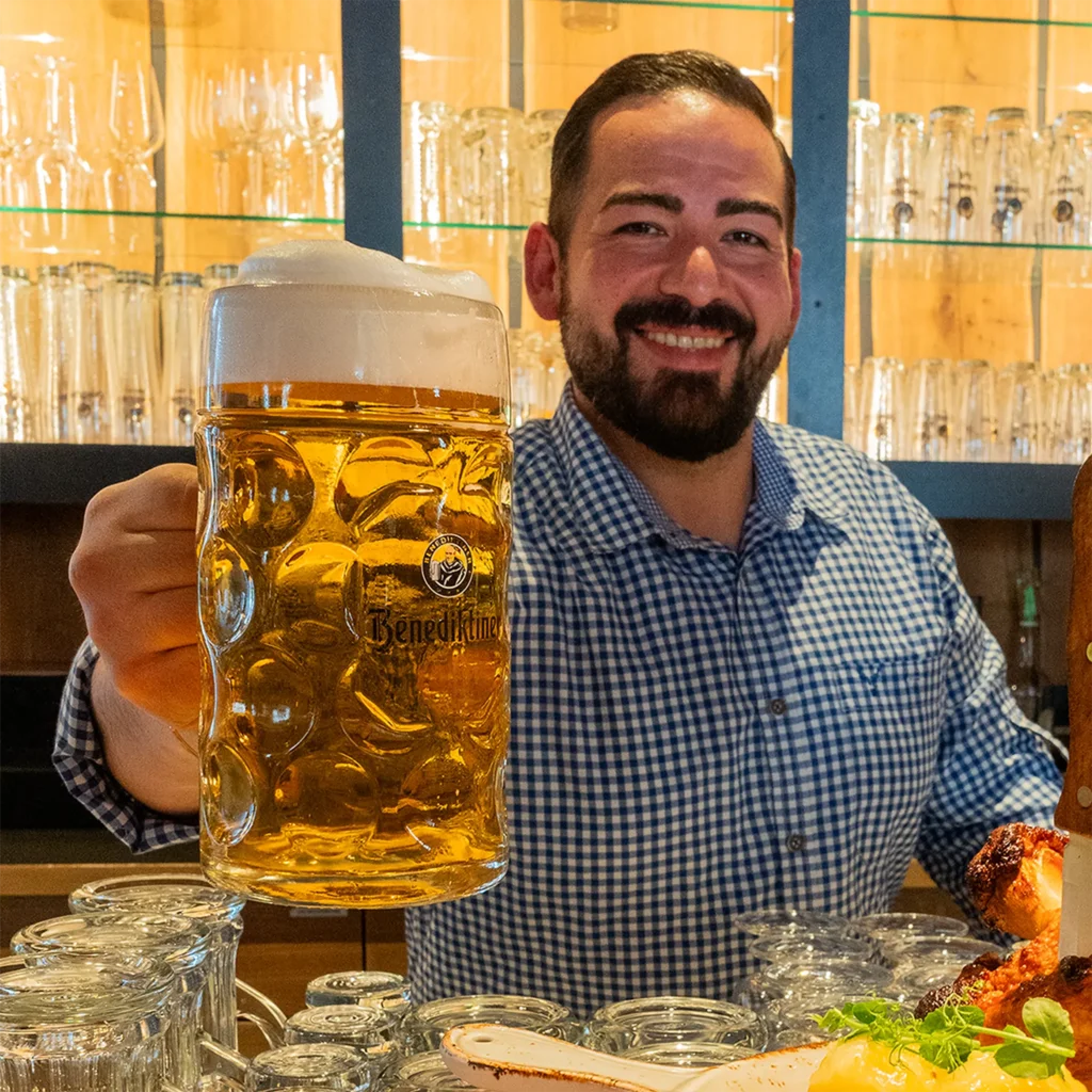 Ein Mitarbeiter im karierten Hemd hält ein Helles in Richtung der Kamera